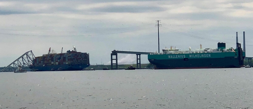MV Carmen hjelpes forbi ulykkesstedet av taubåter fredag 26. april, nøyaktig en måned etter at broen kollapset. Containerskipet MV Dali står fortsatt igjen på ulykkesstedet.